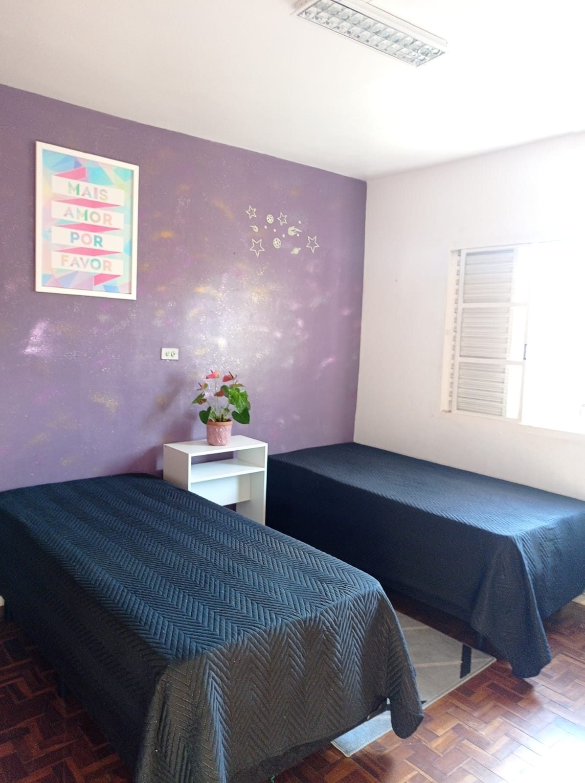 Quarto compartilhado do Second Home com parede lilás e duas camas
