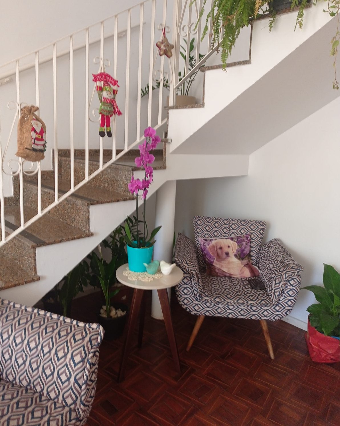 Sala do Second Home com poltronas estampadas, mesa lateral com orquídea e escada branca ao fundo