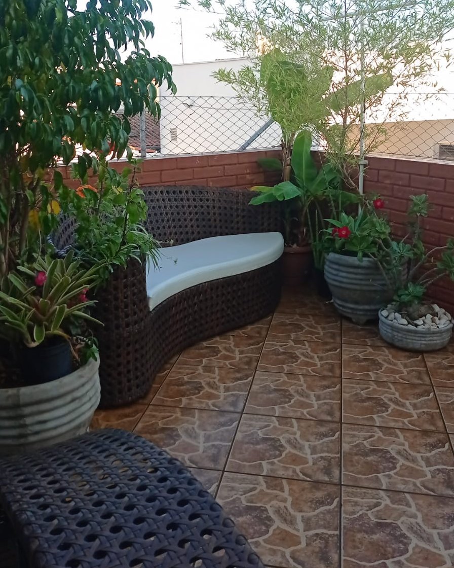 Varanda do Second Home Coliving, com sofá de fibra, plantas e piso de ladrilho